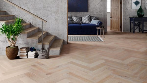 Hallway with W-patterned light-cream flooring leading to a pale grey staircase and a living room with a navy-blue couch